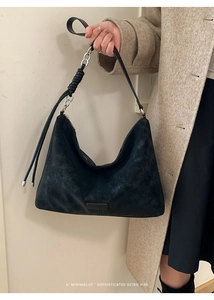 Détail du sac hobo en daim noir avec chaîne argentée et nœud sur un manteau beige