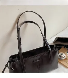 Detail view of smooth brown leather tote bag with thin shoulder straps and metallic hardware