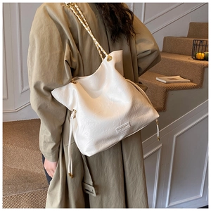Detail of white bucket bag with glossy texture and chain strap worn with khaki trench coat