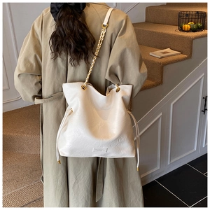 Detail view of white bucket bag featuring gold chain strap and drawstring closure
