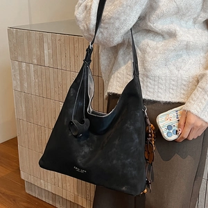 Detail of minimalist black matte suede hobo bag with silver logo worn on shoulder