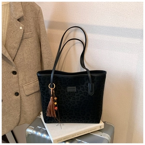 Detail of leopard print tote bag with brown tassel charm and metallic brand plaque