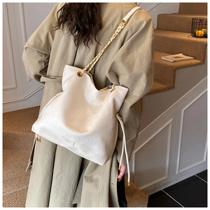 Close-up of a white bucket bag with woven gold chain strap on a trench coat model