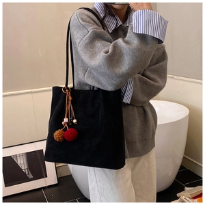 Detail of a black suede tote bag featuring a decorative plush ball charm on a shoulder strap