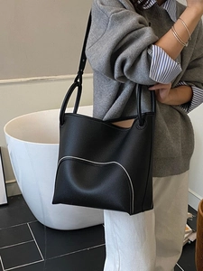 Minimalist black leather bucket bag with silver wavy stitching on a shoulder model