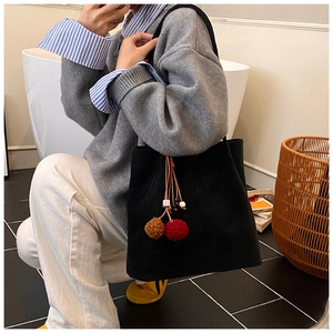Detail of black suede tote bag with decorative plush pom-poms shown in a lifestyle setting