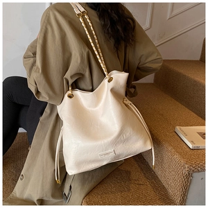Close-up of cream leather bucket bag showing drawstring closure and metal chain strap
