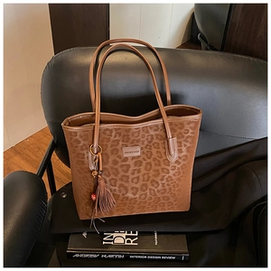 Close-up of leopard print tote bag with metal tassel charm on a black leather chair