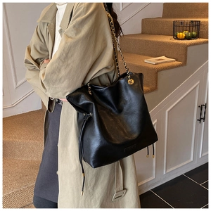 Detail of black leather bucket tote with gold chain strap and drawstring side tassel