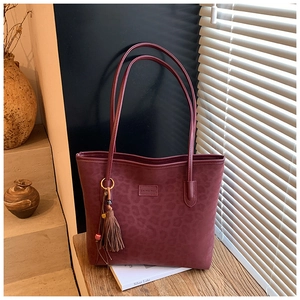 Detail of burgundy leopard print tote bag with stylish tassel and logo on wood