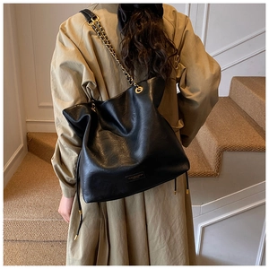 Detail of black faux leather tote bag with metal chain strap on model in beige coat