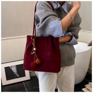 Detail of burgundy faux suede tote bag featuring a decorative two-tone pompom tassel charm