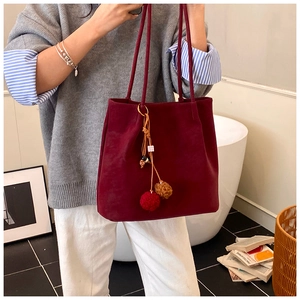 Detail of burgundy suede tote bag with decorative red and brown fur pompom charms