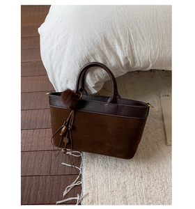 Detail of suede and leather patchwork tote with fuzzy ball charm and wooden bead tassel
