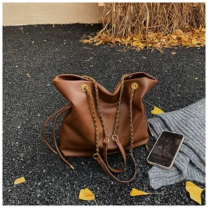Detailed view of brown bucket bag with gold chain strap on autumn gravel background