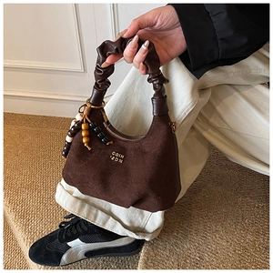 Detailed macro view of dark coffee suede handbag with leather pleated handle and gold logo