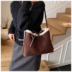 Detail of suede bucket bag with white faux fur trim and bow charm in a soft studio setting
