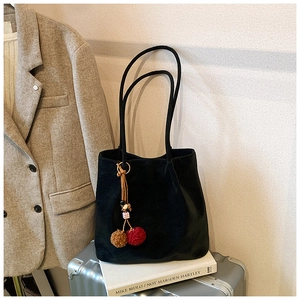 Detail of a black suede tote bag with a reddish-brown plush charm on a suitcase