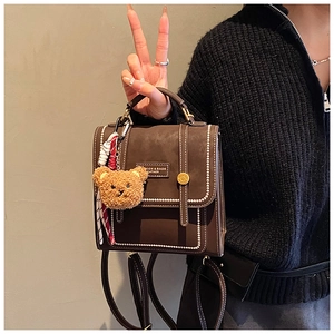 Retro brown leather backpack with contrast stitching and a cute teddy bear charm