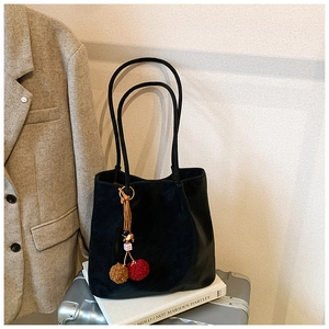 Detail view of black faux suede tote bag with decorative plush charms on a travel suitcase