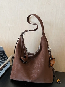 Vintage brown suede tote bag with flower charm and adjustable strap on a minimalist desk