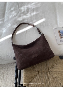 Détail du sac hobo en daim marron avec anneaux métalliques et patch logo vintage
