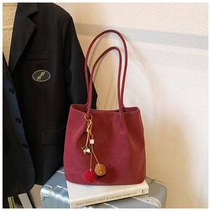 Close-up of dark red suede tote bag with bohemian tassel charm on a travel suitcase