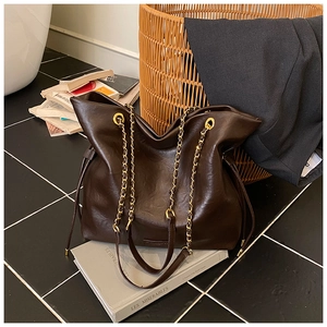 Detail of dark brown leather tote featuring gold chain straps and drawstring side closure