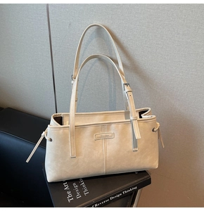 Detail of cream white leather shoulder bag featuring vertical stitching and adjustable straps