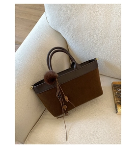 Dettaglio di borsa tote in pelle scamosciata marrone scuro con nappa su divano