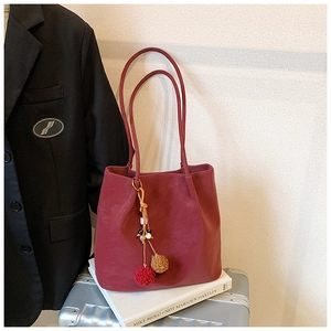 Detail of burgundy suede tote bag with pom-pom charm on art book and silver suitcase