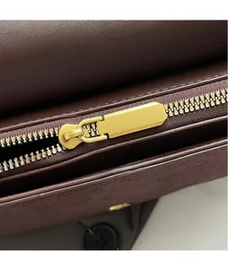 Macro detail of smooth gold hardware zipper on a dark brown leather crossbody bag