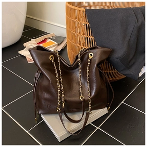 Close-up of matte leather texture, golden chain strap, and drawstring of the brown bucket bag