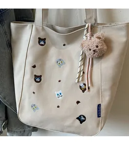 Detail of beige canvas tote featuring cat embroidery and a brown plush bear charm
