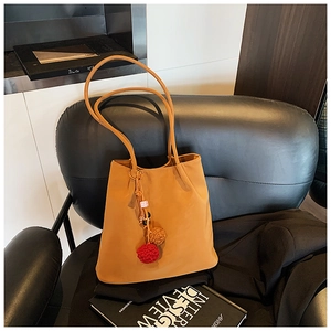Detail of mustard yellow suede tote bag featuring slim shoulder straps and plush pendant
