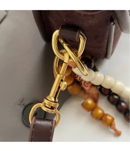 Close-up of vintage golden hook and beaded charm on dark brown frosted leather handbag
