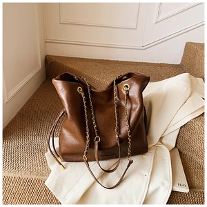 Detail of a large brown bucket bag featuring gold chain handle and pebbled leather texture