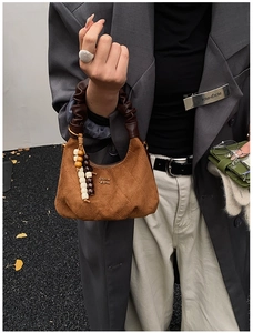 Detail of quilted brown suede bag with ruched handle and decorative beaded pendant