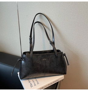 Detail shot of black leather shoulder bag with side drawstrings and metal logo plaque