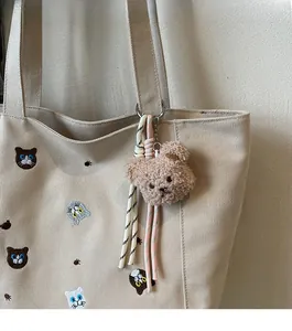 Close-up of plush teddy bear charm with braided cords on a white canvas tote bag
