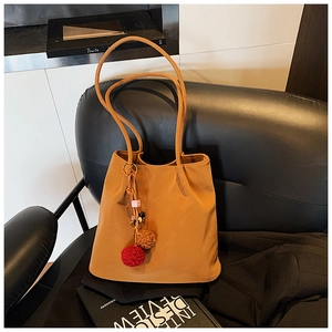 Detail of camel suede tote bag on leather chair with stylish plush ball charm accent