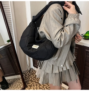 Detail of black quilted puffer crossbody bag with heart pattern and white label on strap