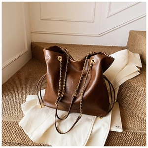 Detail of a large coffee brown leather bucket bag with gold chain strap on a white blazer