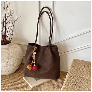 Detail of dark brown suede tote bag with plush pom-poms against a white relief wall