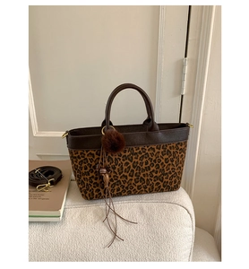 Detail of leopard print tote with brown leather trim, fuzzy ball charm and long tassel