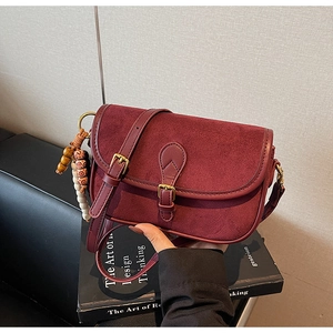 Detail of burgundy crossbody bag with matte texture, gold snap, and wooden bead charm