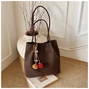 Brown suede tote bag with geometric wood beads and yarn charm on a minimalist background