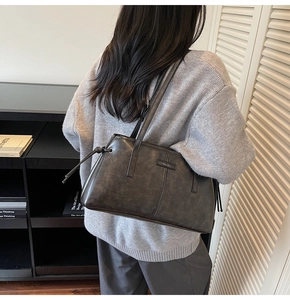 Detail of a retro dark gray leather shoulder bag with vertical stitching and metal logo