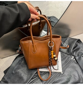 Détail d'un sac seau en cuir marron avec garnitures argentées et breloque pompon perlé