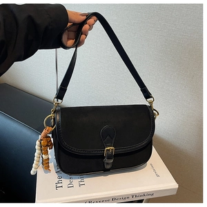 Detail of vintage black saddle bag with suede texture and wooden bead charm accessory